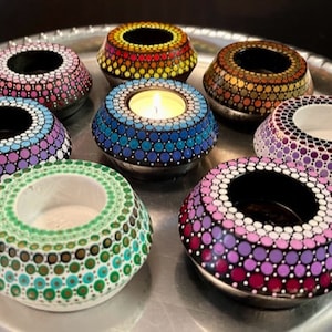 May include: Eight tealight candle holders with a polka dot design in various colors, including purple, blue, green, orange, and pink. The candle holders are arranged in a circle on a silver tray.