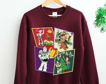May include: Burgundy sweatshirt with a Christmas-themed design featuring characters from the Toy Story franchise. The design includes Woody, Buzz Lightyear, Jessie, and Rex.