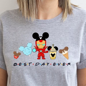 May include: Gray t-shirt with a cartoon image of Iron Man wearing Mickey Mouse ears and holding a Mickey Mouse ice cream cone. The text "BEST DAY EVER" is printed below the image.