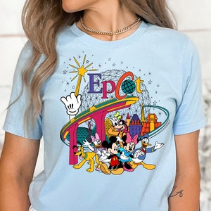 May include: Light blue t-shirt with a graphic of Mickey Mouse and friends in front of the Epcot Center. The graphic includes the Epcot logo and the iconic Spaceship Earth.