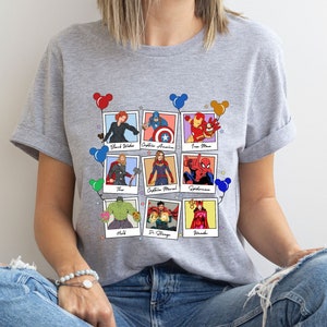 May include: Gray t-shirt with a colorful graphic of Marvel characters in Polaroid frames with Mickey Mouse ears. The characters include Black Widow, Captain America, Iron Man, Thor, Captain Marvel, Spiderman, Hulk, Dr. Strange, and Wanda.