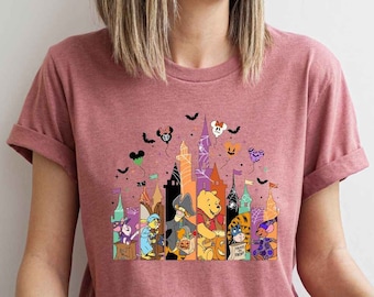 Może przedstawiać: Różowa koszulka z grafiką przedstawiającą zamek Disney'a w stylu Halloween z Winniem the Poohem i innymi postaciami. Zamek jest ozdobiony nietoperzami, dyniami i pajęczynami.