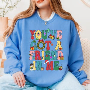 A woman wearing a blue sweatshirt with a colorful graphic design that says "YOU'VE GOT A FRIEND IN ME"