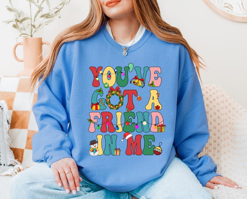 A woman wearing a blue sweatshirt with a colorful graphic design that says "YOU'VE GOT A FRIEND IN ME"