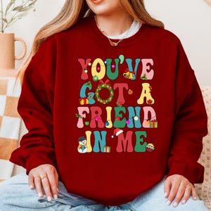 A woman wearing a red sweater with the text "YOU'VE GOT A FRIEND IN ME" printed on it.