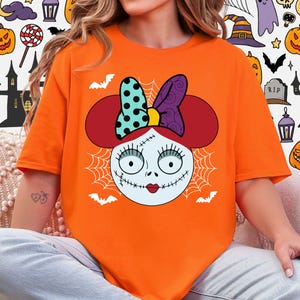 A person wearing an orange t-shirt with a cartoon-style illustration of a female character with a bow on her head, resembling the character Sally from the movie Sally's Monster.