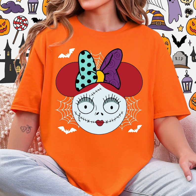 A person wearing an orange t-shirt with a cartoon-style illustration of a female character with a bow on her head, resembling the character Sally from the movie Sally's Monster.