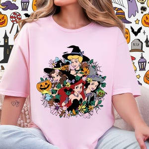 A woman wearing a pink t-shirt with a graphic design featuring cartoon characters surrounded by flowers and Halloween-themed elements.