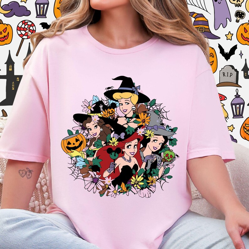 A woman wearing a pink t-shirt with a graphic design featuring cartoon characters surrounded by flowers and Halloween-themed elements.