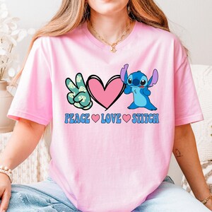 A woman wearing a pink t-shirt with a peace sign and a heart, along with the text "PEACE LOVE STITCH".