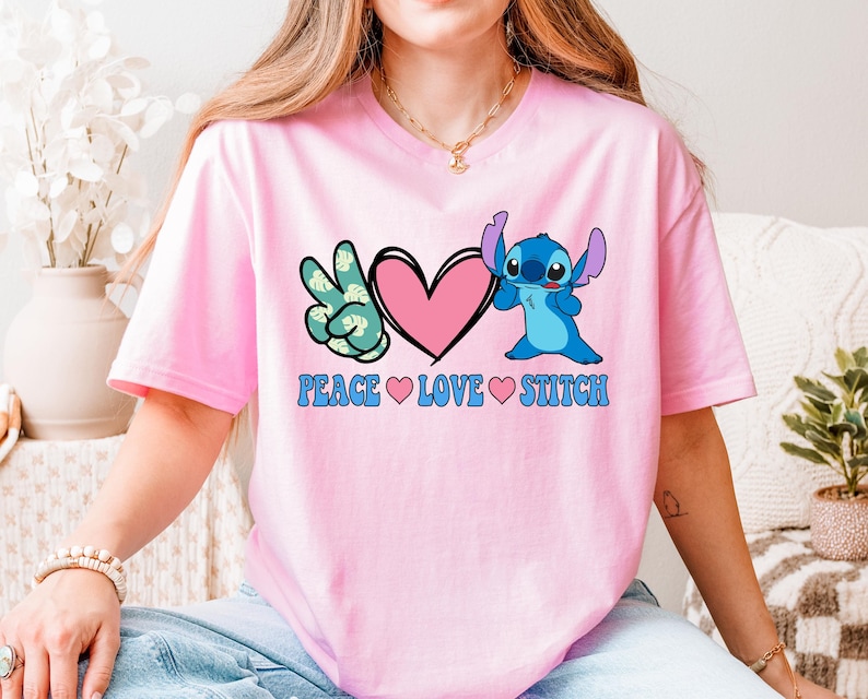 A woman wearing a pink t-shirt with a peace sign and a heart, along with the text "PEACE LOVE STITCH".