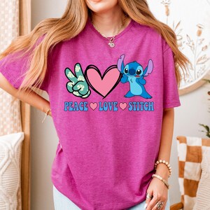 A woman wearing a pink t-shirt with a peace sign and a heart, along with the text "PEACE LOVE STITCH".