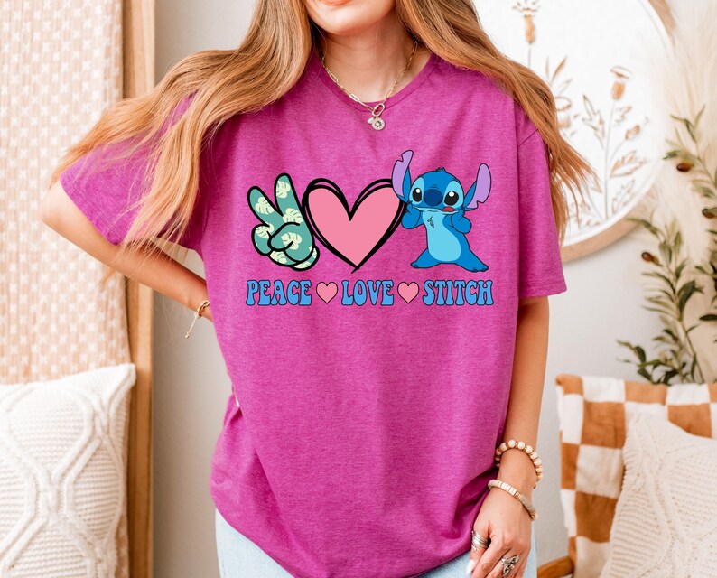 A woman wearing a pink t-shirt with a peace sign and a heart, along with the text "PEACE LOVE STITCH".