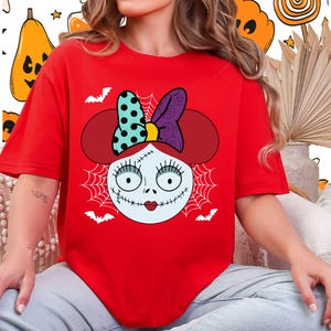 A woman wearing a red t-shirt with a cartoon design of a smiling face with a bow on her head.