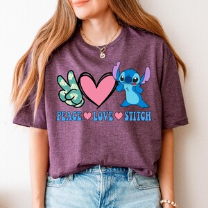 A woman wearing a purple t-shirt with a graphic design featuring a character from the Lilo & Stitch movie franchise, along with the text "Peace Love Stitch".