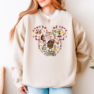 A woman wearing a beige sweater with a large, colorful, cartoonish design of various characters and objects, including a snowman, reindeer, and other festive elements.