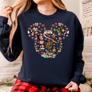 A woman wearing a navy blue sweatshirt with a colorful, pixelated design of various Christmas-themed characters and symbols.