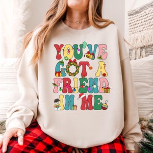 A woman wearing a white sweatshirt with a colorful text design that says "You've Got a Friend in Me".