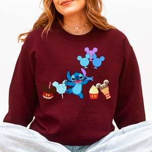A woman wearing a burgundy sweater with a cartoon character and various Disney-themed items printed on it.
