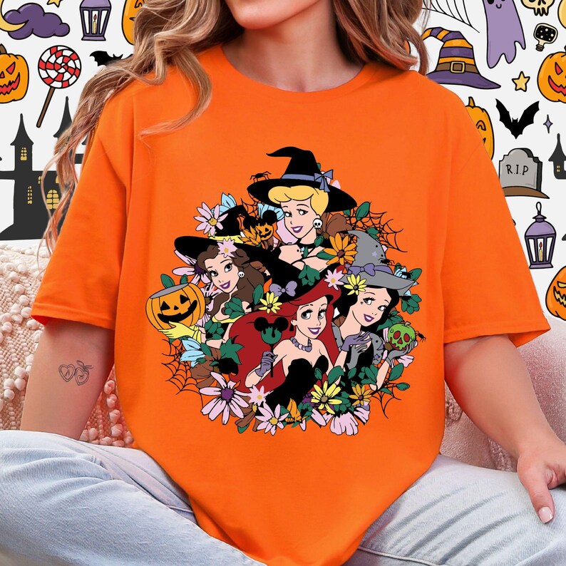 A person wearing an orange t-shirt with a graphic design featuring cartoon characters and Halloween-themed elements.