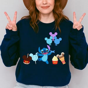 A woman wearing a blue sweatshirt with a cartoon character and various Disney-themed items printed on it.