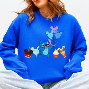 A woman wearing a blue sweatshirt with a cartoon character and various Disney-themed items printed on it.