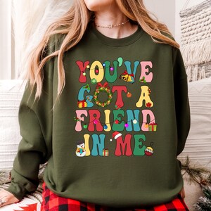 A woman wearing a green sweatshirt with a colorful text design that says "YOU'VE GOT A FRIEND IN ME" printed on it.