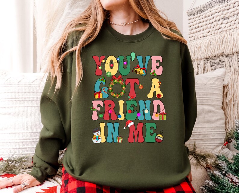 A woman wearing a green sweatshirt with a colorful text design that says "YOU'VE GOT A FRIEND IN ME" printed on it.