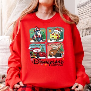 A person wearing a red sweater with a Disney Cars Christmas-themed design featuring four cartoon characters.