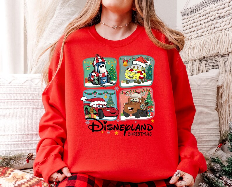 A person wearing a red sweater with a Disney Cars Christmas-themed design featuring four cartoon characters.