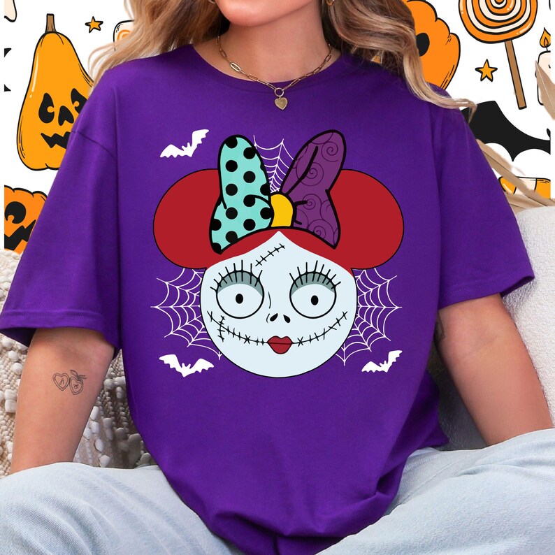A person wearing a purple t-shirt with a graphic design featuring a cartoon-style face with a bow, spider web, and bats.