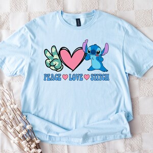 A light blue t-shirt with a peace sign and a heart graphic, along with the text "Peace Love Stitch" printed on it.