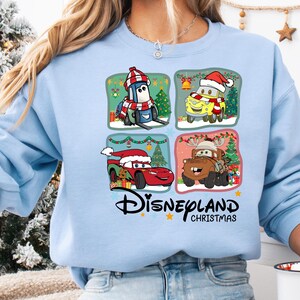 A woman wearing a blue sweatshirt with a graphic design featuring four cartoon characters from the Disney movie Cars, including a car, a truck, a penguin, and a snowman.