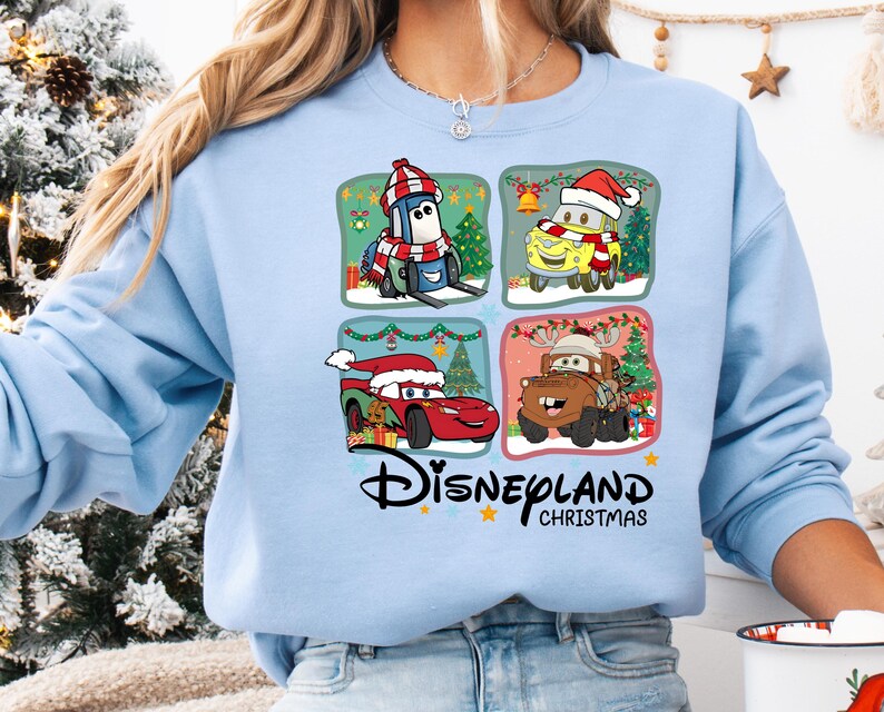 A woman wearing a blue sweatshirt with a graphic design featuring four cartoon characters from the Disney movie Cars, including a car, a truck, a penguin, and a snowman.