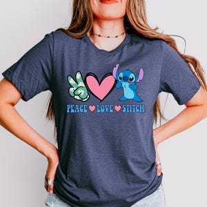 A woman wearing a gray t-shirt with a graphic design featuring a character from the Lilo & Stitch movie franchise and the text "Peace Love Stitch".