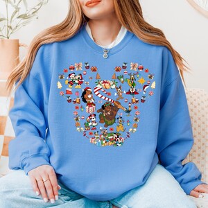 A woman wearing a blue sweatshirt with a large, colorful design featuring various Disney characters and holiday-themed elements.