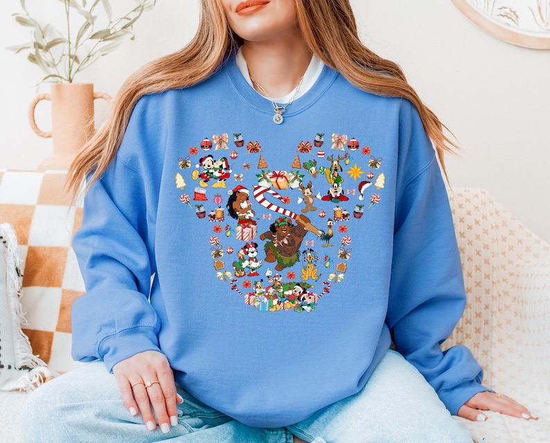A woman wearing a blue sweatshirt with a large, colorful design featuring various Disney characters and holiday-themed elements.