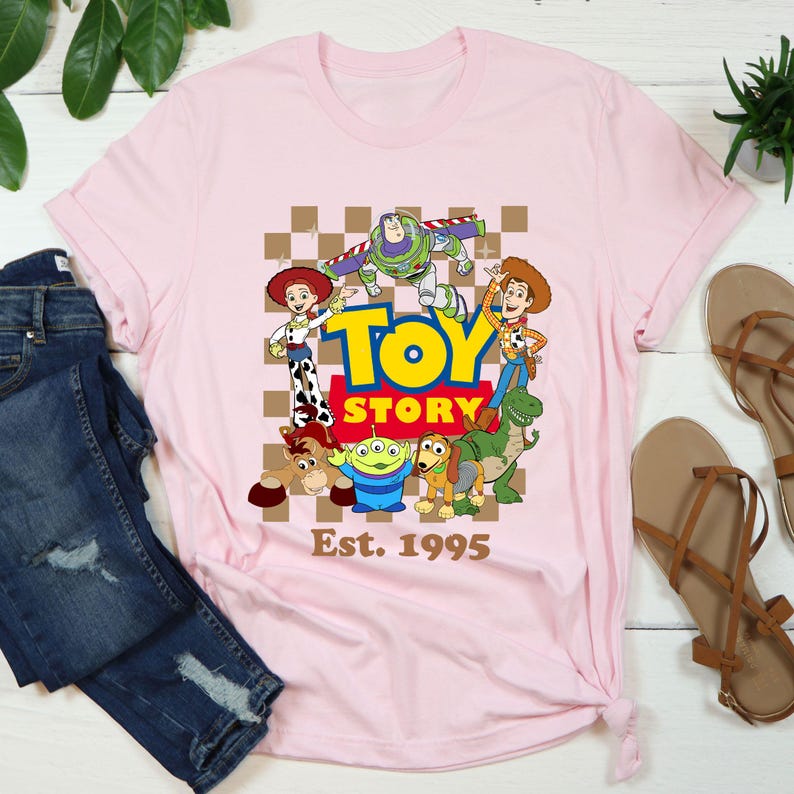a pink toy story t - shirt sitting on top of a pair of jeans
