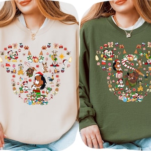 two women wearing sweaters with a Mickey Mouse theme. The sweaters are decorated with various Disney characters and holiday-themed elements, such as snowflakes, presents, and Christmas trees.