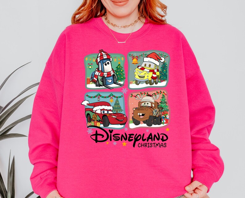 A woman wearing a pink sweatshirt with a collage of four Disney Cars characters from the movie "Disneyland Christmas" on it.