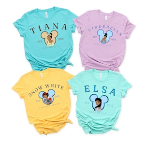 Puede incluir: Cuatro camisetas diferentes con princesas de Disney. Cada camiseta tiene una princesa diferente, una silueta de oreja de Mickey Mouse, el nombre de la princesa y el a&ntilde;o de su fundaci&oacute;n. Las camisetas son de color turquesa, lavanda, amarillo y azul claro.
