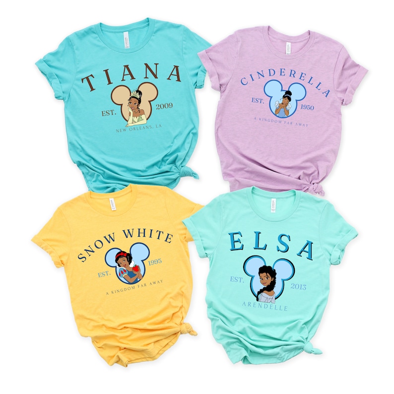 Puede incluir: Cuatro camisetas diferentes con princesas de Disney. Cada camiseta tiene una princesa diferente, una silueta de oreja de Mickey Mouse, el nombre de la princesa y el a&ntilde;o de su fundaci&oacute;n. Las camisetas son de color turquesa, lavanda, amarillo y azul claro.