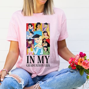 a woman wearing a pink t - shirt that says in my graduation era