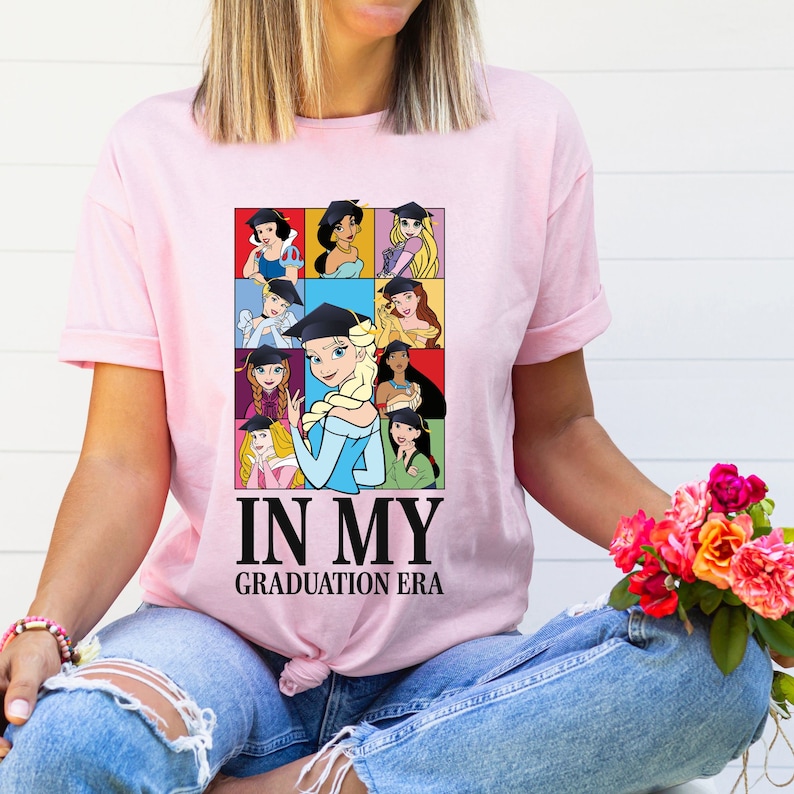 a woman wearing a pink t - shirt that says in my graduation era