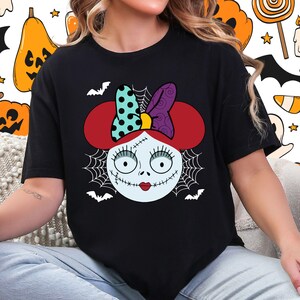 A woman wearing a black t-shirt with a graphic design featuring a cartoon-style face with a bow, spider web, and bats.