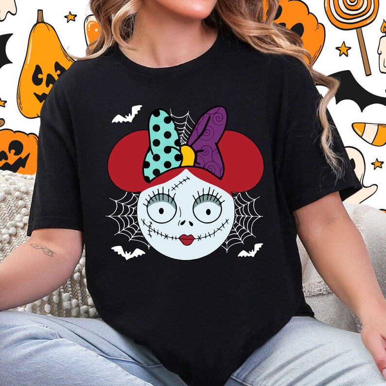A woman wearing a black t-shirt with a graphic design featuring a cartoon-style face with a bow, spider web, and bats.