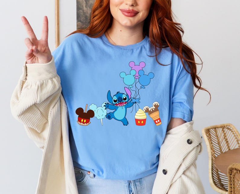 A woman wearing a blue t-shirt with a cartoon character and various Disney-themed items, such as Mickey Mouse and cotton candy, printed on it.