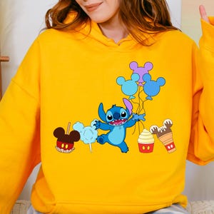 A person wearing a yellow hoodie with a cartoon character and various Disney-themed items printed on it.