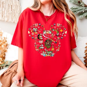 A person wearing a red t-shirt with a Mickey Mouse design is sitting in front of Christmas decorations.