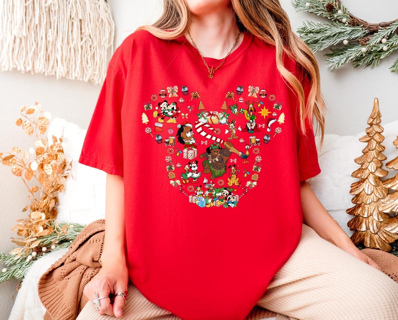 A person wearing a red t-shirt with a Mickey Mouse design is sitting in front of Christmas decorations.